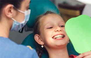 Child with retainer smiling at reflection in handheld mirror