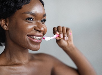 Closeup of woman with braces smiling while brushing her teeth