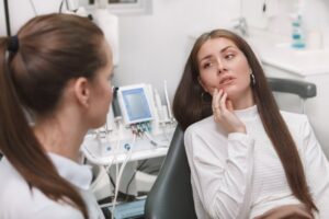 Young woman pointing to jaw while sitting in dentist's chair.